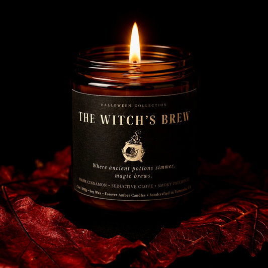 Lit The Witch’s Brew 7 oz soy candle from the Forever Amber Candles Halloween Collection surrounded by red autumn leaves
